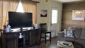 A living room with a television on a wooden cabinet, a couch, a chair, and a small table with a magazine.