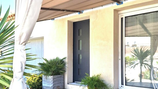 A covered patio area with a sliding glass door, potted plants, and a curtain. - LA Magdeleine (Cabannes)