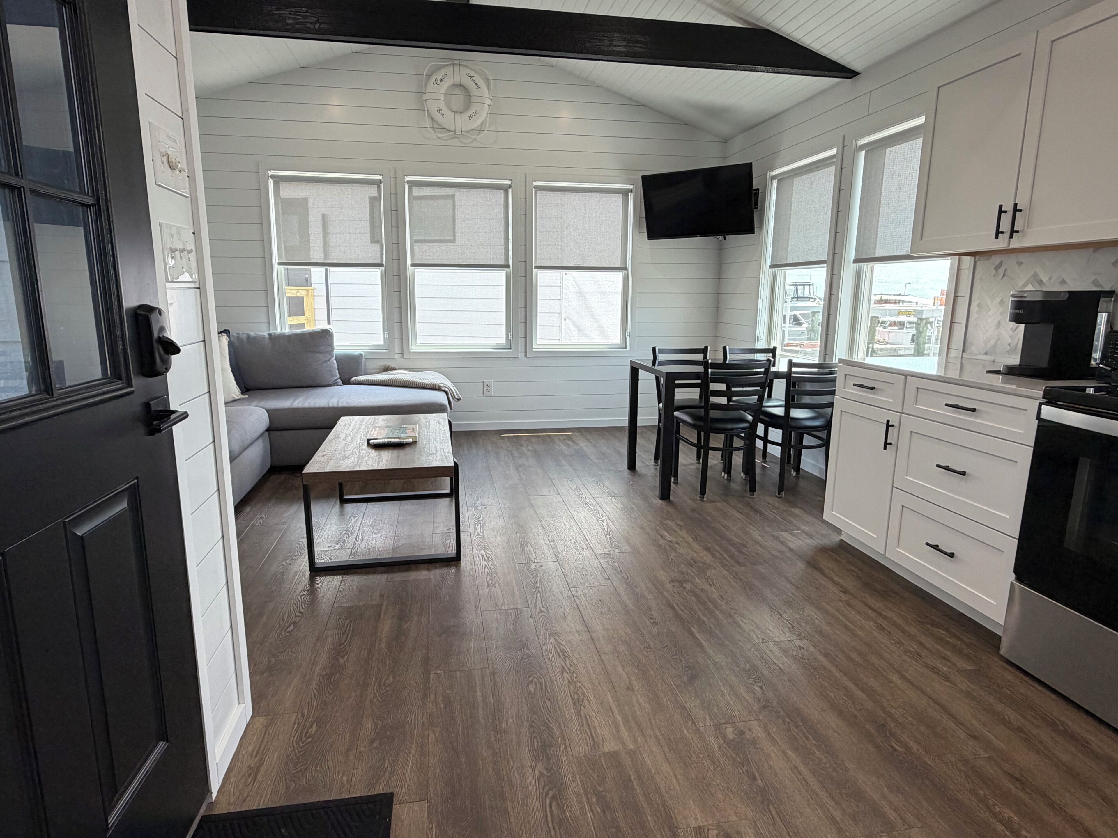 A modern kitchen with white cabinetry, a dining area with a table and chairs, a built-in TV, and a large window.