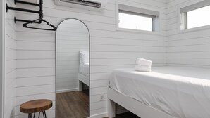 A white room with a bed, a mirror, and a wooden stool.