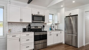 A modern kitchen with white cabinets, stainless steel appliances, and a herringbone tile backsplash.