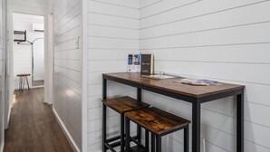 A narrow hallway with white paneled walls and a wooden floor. There is a small table with a magazine and a box on it.