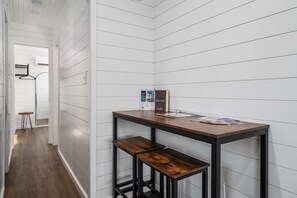 Un pasillo estrecho con paredes blancas con paneles y piso de madera. Hay una pequeña mesa con una revista y una caja encima.