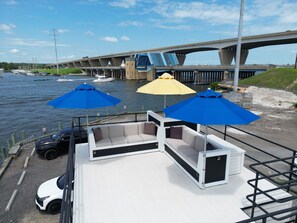 A boat with outdoor seating and umbrellas, docked near a bridge over water.