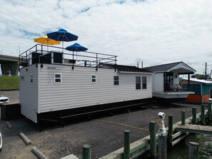 Una casa flotante anclada en un muelle, con una pequeña terraza y zona cubierta.