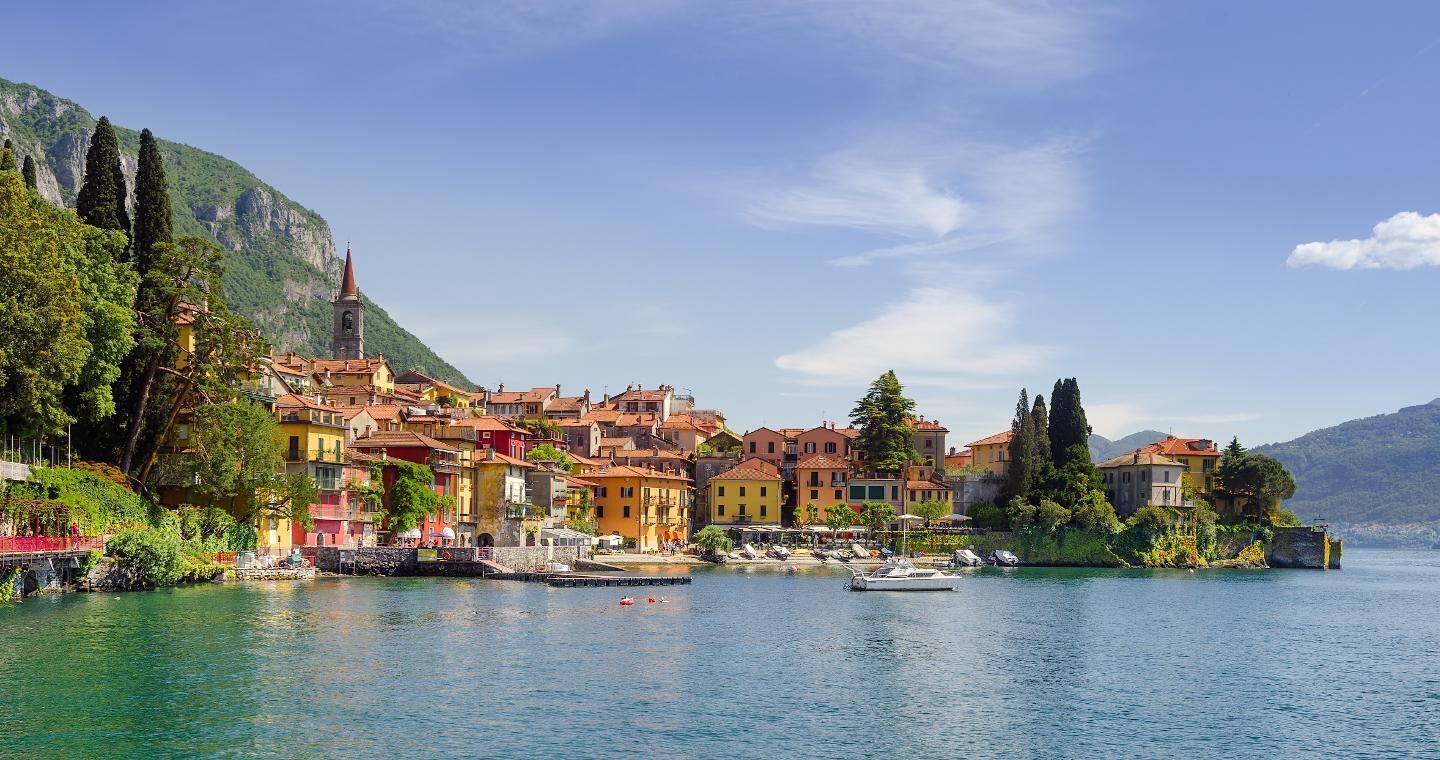 Un pittoresco paese sul lago, con edifici colorati, una chiesa e barche sull'acqua.