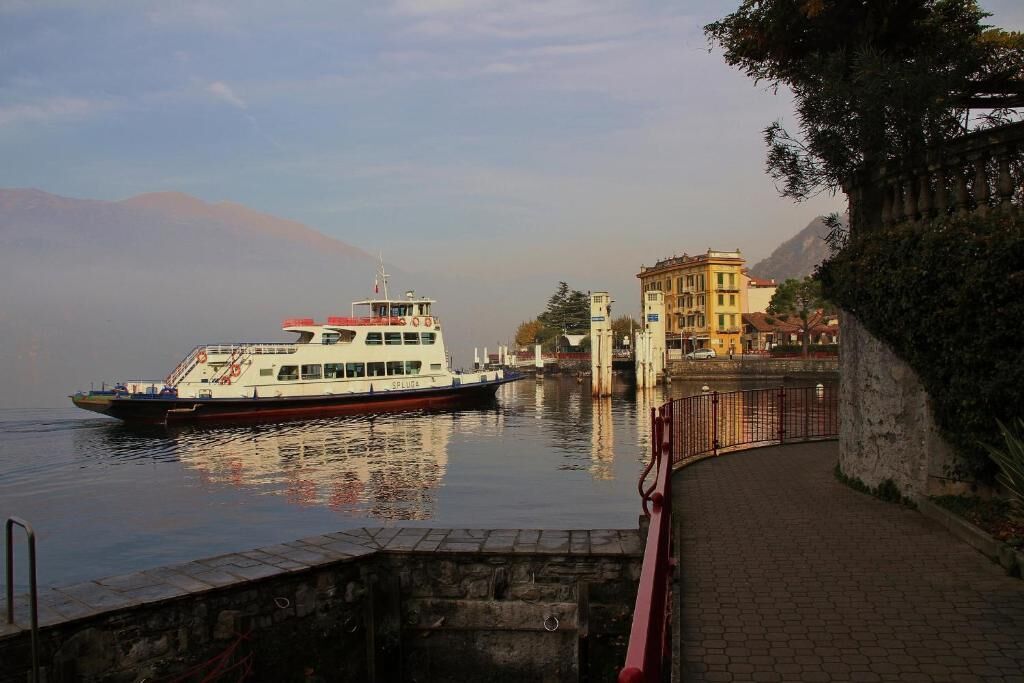 Un traversier accosta dans un port bordé d’un mur de pierre et d’une promenade pavée.