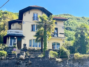 Un immeuble à plusieurs étages doté de balcons, d’un escalier en pierre et d’une végétation luxuriante en arrière-plan.