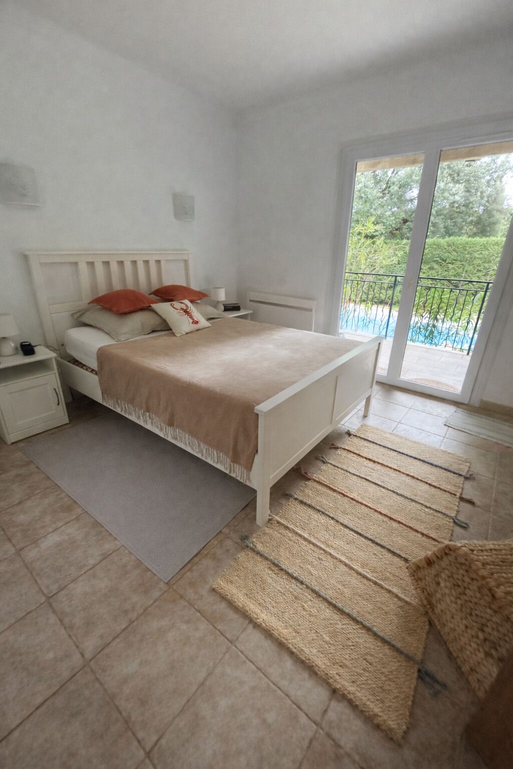 A bedroom with a bed, nightstands, a window, and a view of a balcony.