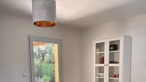 A dining area with a table, chairs, a hanging light fixture, a cabinet, and a door leading to an outdoor area.