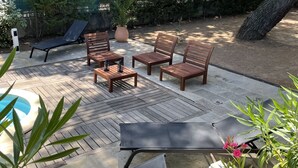 A patio with wooden furniture, including a table and chairs, and a pool in the background.