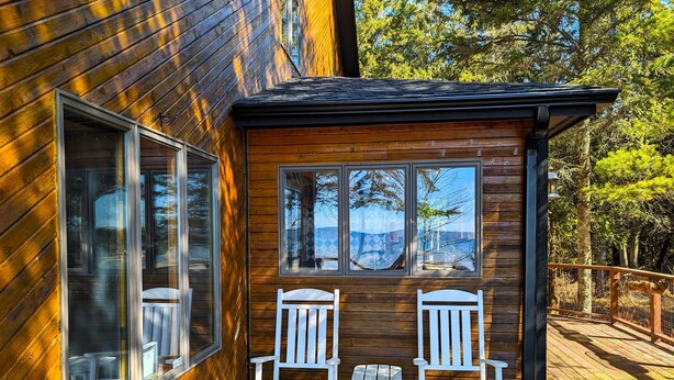 A wooden cabin with a deck, two white Adirondack chairs, and a small table.