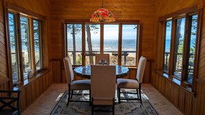 A wooden cabin with a round table and chairs, large windows, and a view of the ocean.