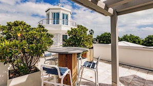 Una terrazza panoramica con un tavolo rotondo e sedie, circondata da piante in vaso e un edificio bianco con un balcone sullo sfondo.