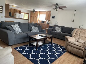 Un salon avec deux canapés gris, une table basse en bois, un fauteuil beige et un tapis bleu à motifs.