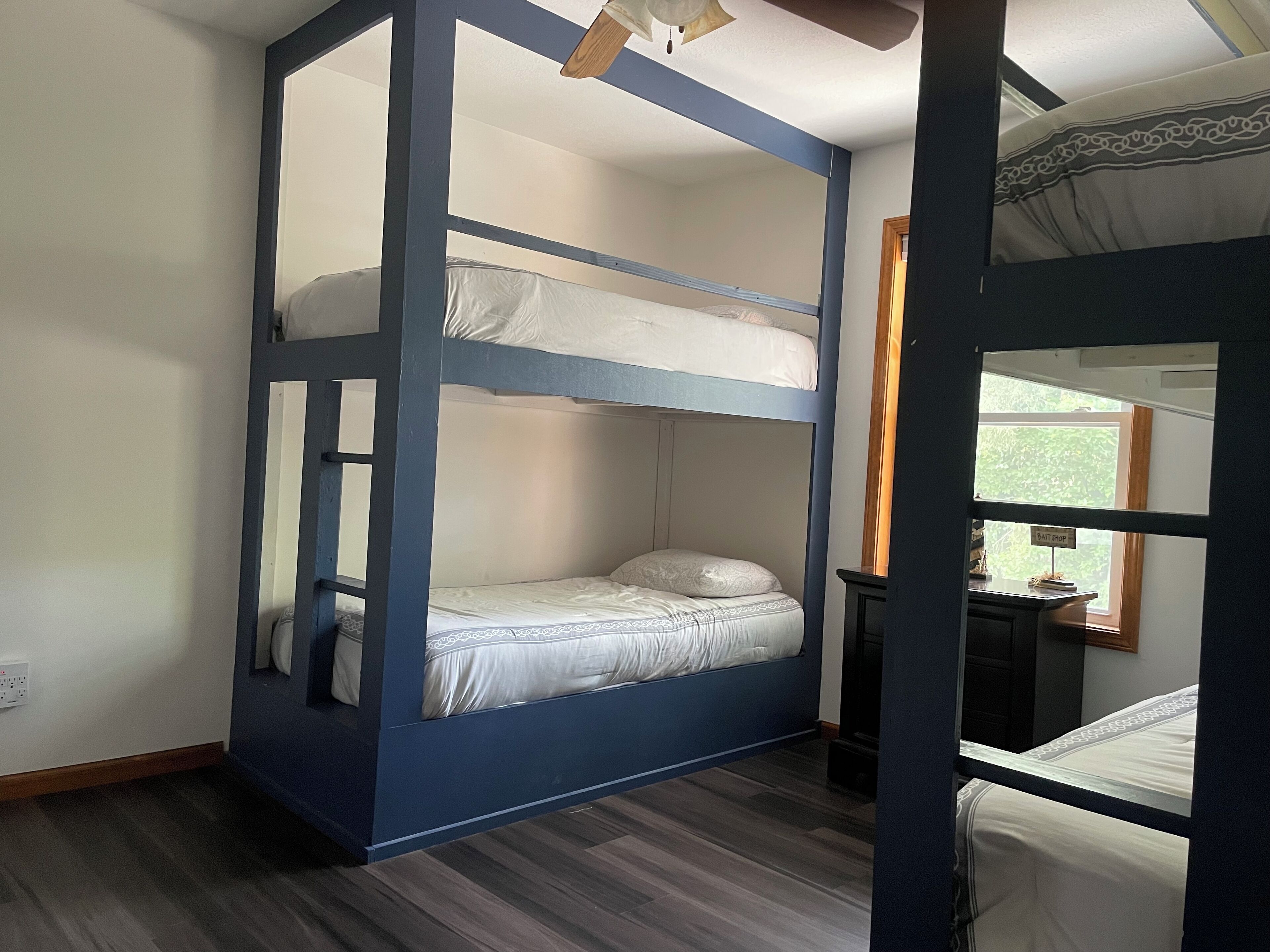Quarto com beliche, uma mesa e uma cadeira, com janela.