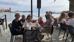 A group of people seated at an outdoor table with a view of the sea and a historic building in the background. - Maison typique catalane (Collioure)
