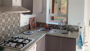 A compact kitchen with a gas stove, a dishwasher, and a window with a view of greenery. - Maison typique catalane (Collioure)