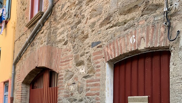 A stone building with two red doors, one with a metal plate above it. - Maison typique catalane (Collioure)