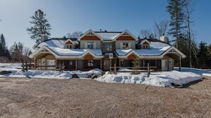 Une grande maison à plusieurs étages, dont le toit est recouvert de neige et qui est bordée d’une allée en gravier.