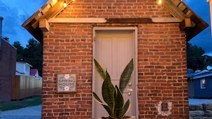 A brick building with a white door, a sign reading "SPRING HOUSE," and a potted plant in front.
