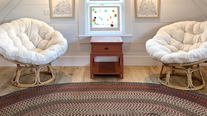 A cozy attic room with a sloped ceiling, two fluffy chairs, a small wooden table, and artwork on the walls.
