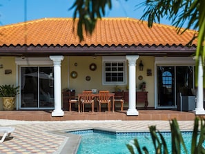 Uma casa com telhado de cerâmica, piscina e um alpendre com cadeiras e uma mesa.