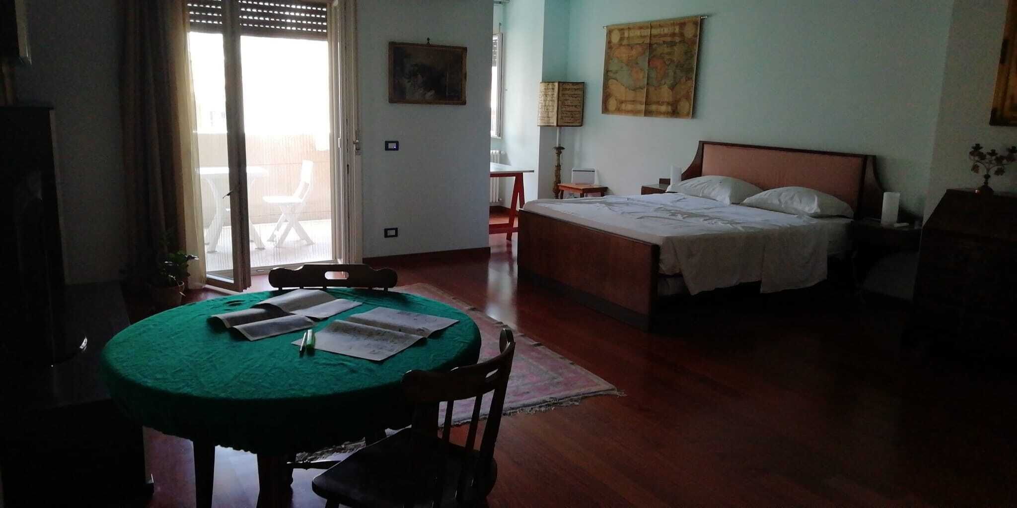 Una habitación con cama, una mesa con papeles, una silla y una ventana con persianas.