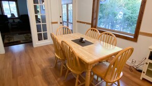 Un coin repas avec une table et des chaises en bois, une fenêtre donnant sur les arbres et une porte menant à une autre pièce.