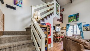 A staircase leading to a second floor, a dining area with a table and chairs, and a living room with a sofa and a lamp.