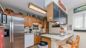 A compact kitchen with wooden cabinets, a stainless steel refrigerator, a coffee maker, and a small island with a chair.