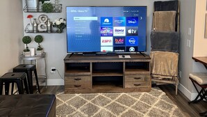 Una sala de estar moderna con televisor de pantalla plana, mueble bajo de madera, otomanas de cuero negro y una alfombra estampada.