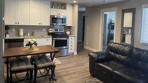 Una cocina moderna con armarios blancos, electrodomésticos de acero inoxidable y un comedor con mesa de madera y sillas acolchadas.