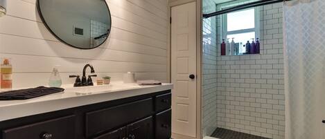 Un bagno con lavandino bianco, mobili scuri, uno specchio rotondo e una cabina doccia con porta in vetro.