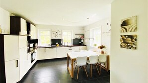 Une cuisine moderne avec des meubles blancs, une table à manger avec des chaises et des œuvres d’art accrochées aux murs.