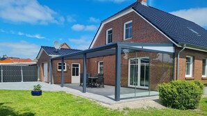 Une maison moderne dotée d’un patio entièrement vitré, d’une façade en briques et d’une pelouse bien entretenue.