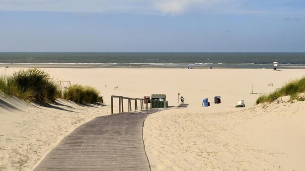 Une promenade en bois menant à une plage de sable, avec une tour de surveillance et des chaises de plage.