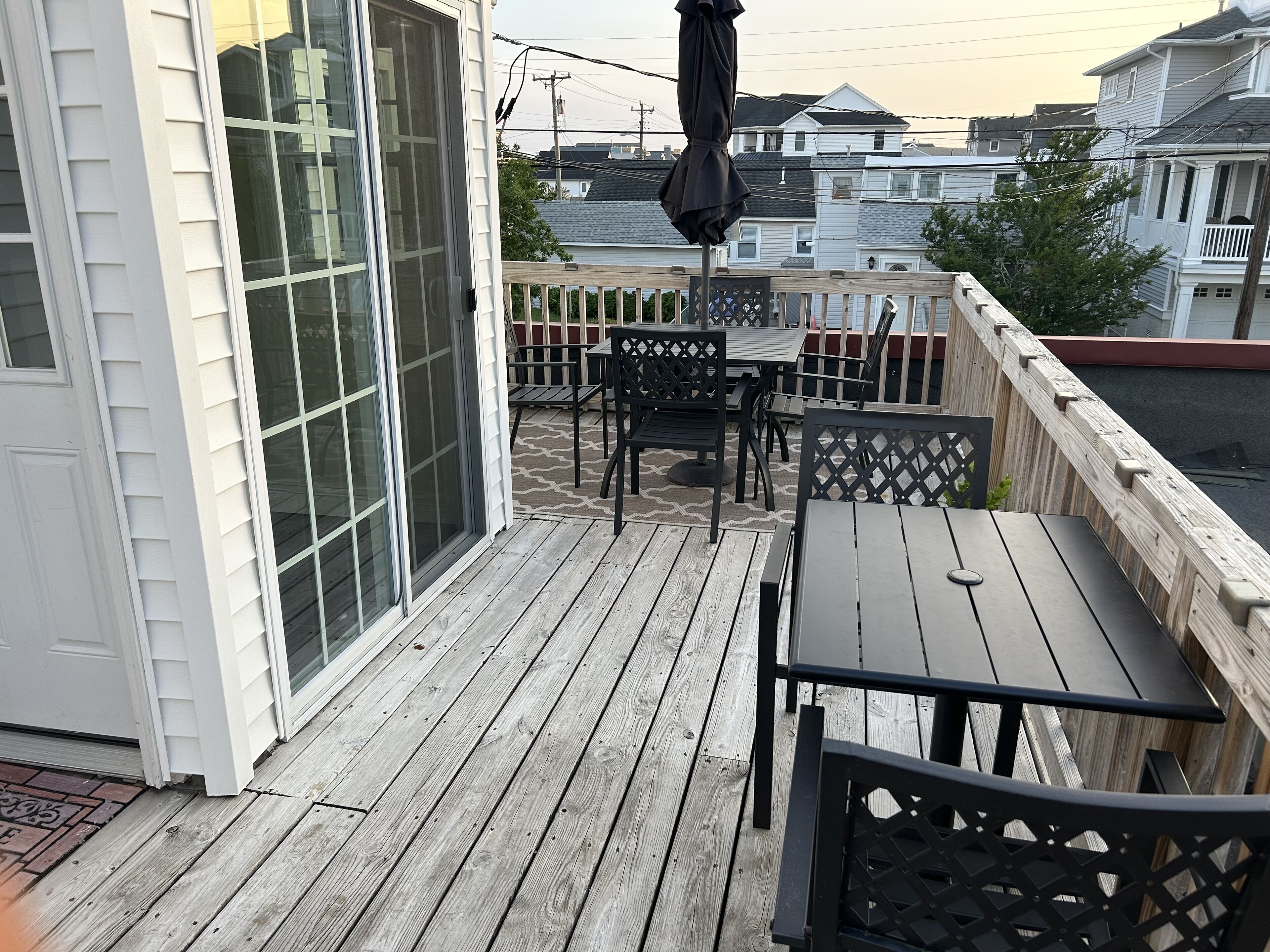 Une terrasse en bois, aménagée avec du mobilier d’extérieur, notamment une table et des chaises, et dotée d’une porte-fenêtre coulissante.