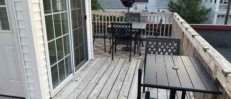 Une terrasse en bois, aménagée avec du mobilier d’extérieur, notamment une table et des chaises, et dotée d’une porte-fenêtre coulissante.