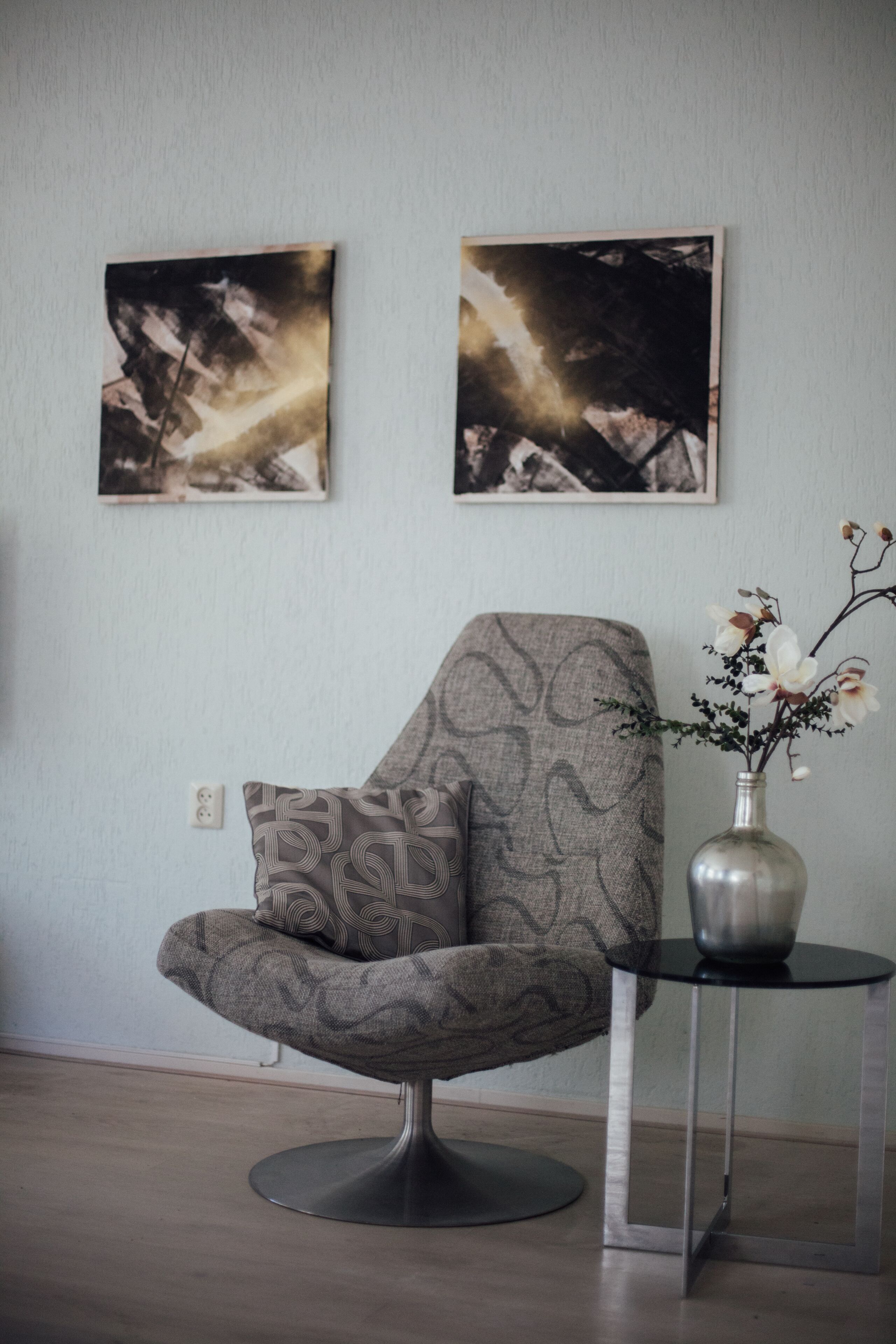Une pièce moderne avec un fauteuil à motifs, une petite table sur laquelle est posé un vase de fleurs, et deux tableaux abstraits accrochés au mur.