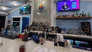 Een bar met diverse drankflessen, glazen en een televisiescherm waarop iemand te zien is.