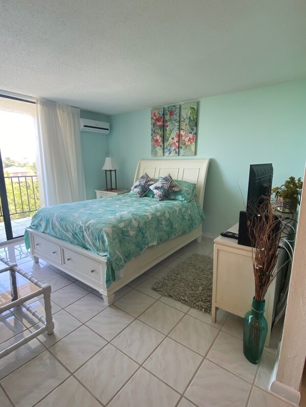 A bedroom with a bed, a nightstand, a chair, a small table, a vase, and a painting on the wall. - A little piece of paradise is waiting for you , 1 minute walk to pool and ocean (Freeport)