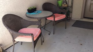 A patio area with wicker chairs and a small table, a welcome sign, and a metal rack with plants. - Close to shopping and freeway access.  (Yuma)