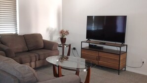A living room with a sofa, a glass coffee table, a TV on a wooden stand, and a ceiling fan. - Close to shopping and freeway access.  (Yuma)