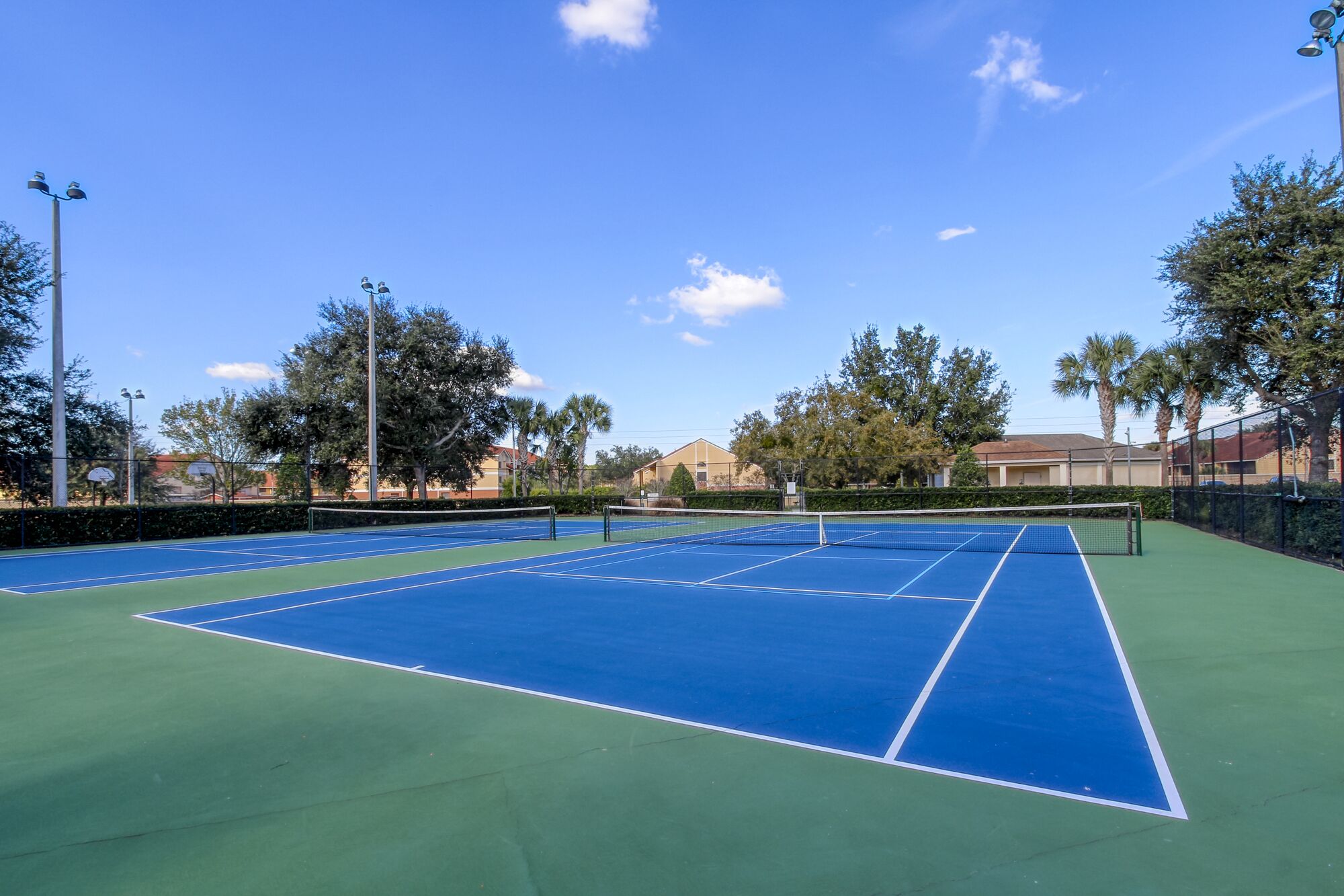 Un court de tennis en plein air, doté d’une surface verte et bleue, entouré d’arbres et de bâtiments.