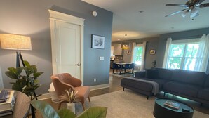 A modern living room with a sofa, armchair, and coffee table. There is a dining area with a table and chairs. The room has a door, a ceiling fan, and a window with curtains. - The Nations Home Close to Downtown (Nashville)