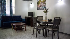 Un salon avec un canapé bleu, une table basse, une table à manger avec des chaises, un téléviseur et un tableau accroché au mur.