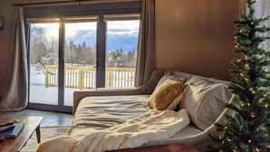 A cozy room with a bed, a Christmas tree, and a view of a snowy deck.