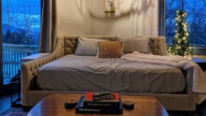 A cozy bedroom with a large bed, a small table with books, and a Christmas tree by the window.