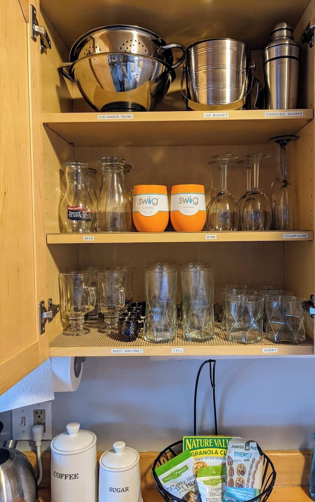 Une cuisine avec des étagères où sont rangés différents types de verrerie, notamment des verres à shooter, des verres à vin et une passoire.